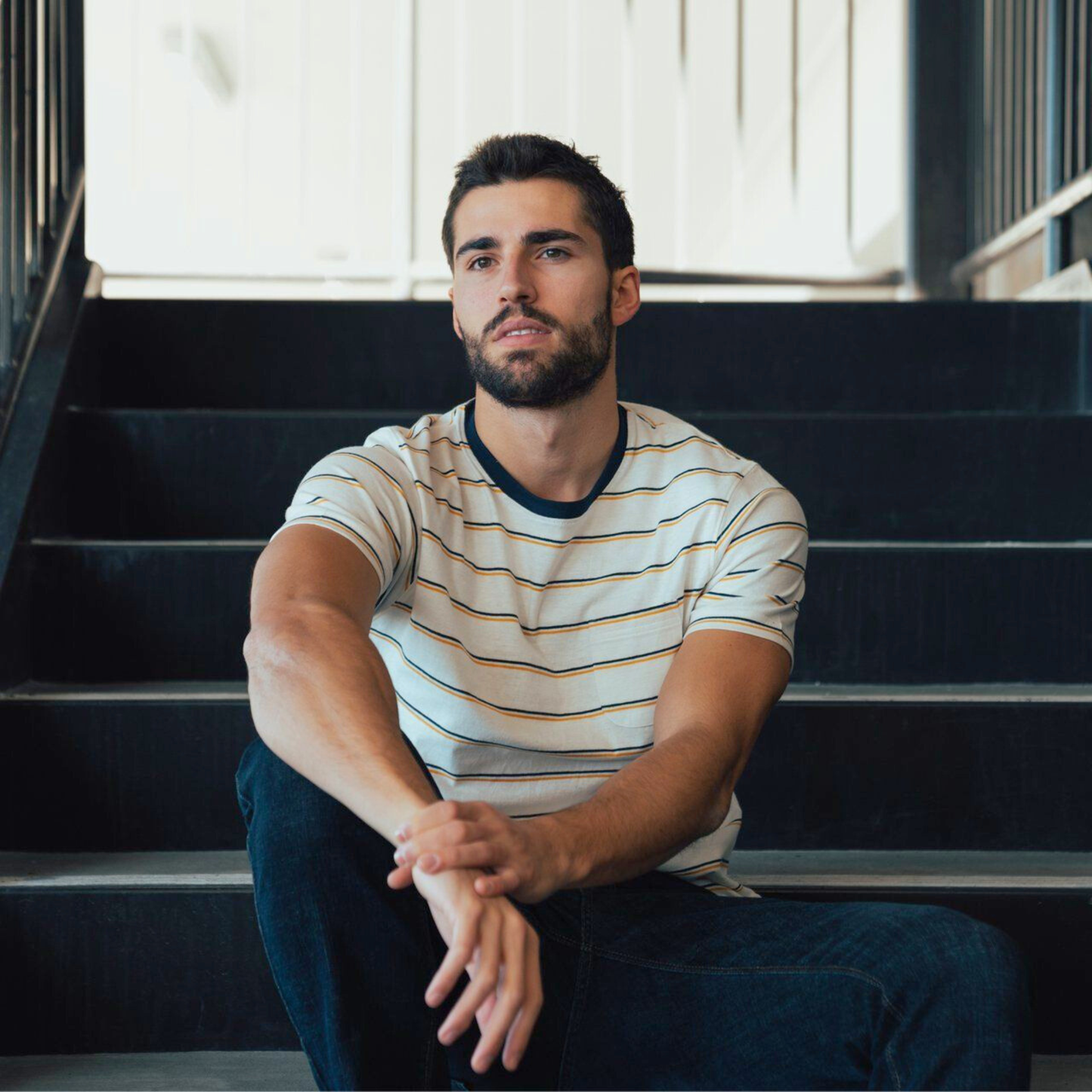 Man sitting on a set of stairs wearing a striped shirt.